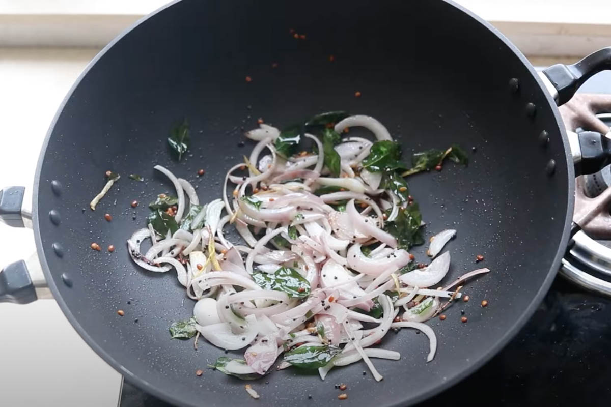 Urad dal, curry leaves, julienned ginger, asafoetida, and sliced red onion added to the pan