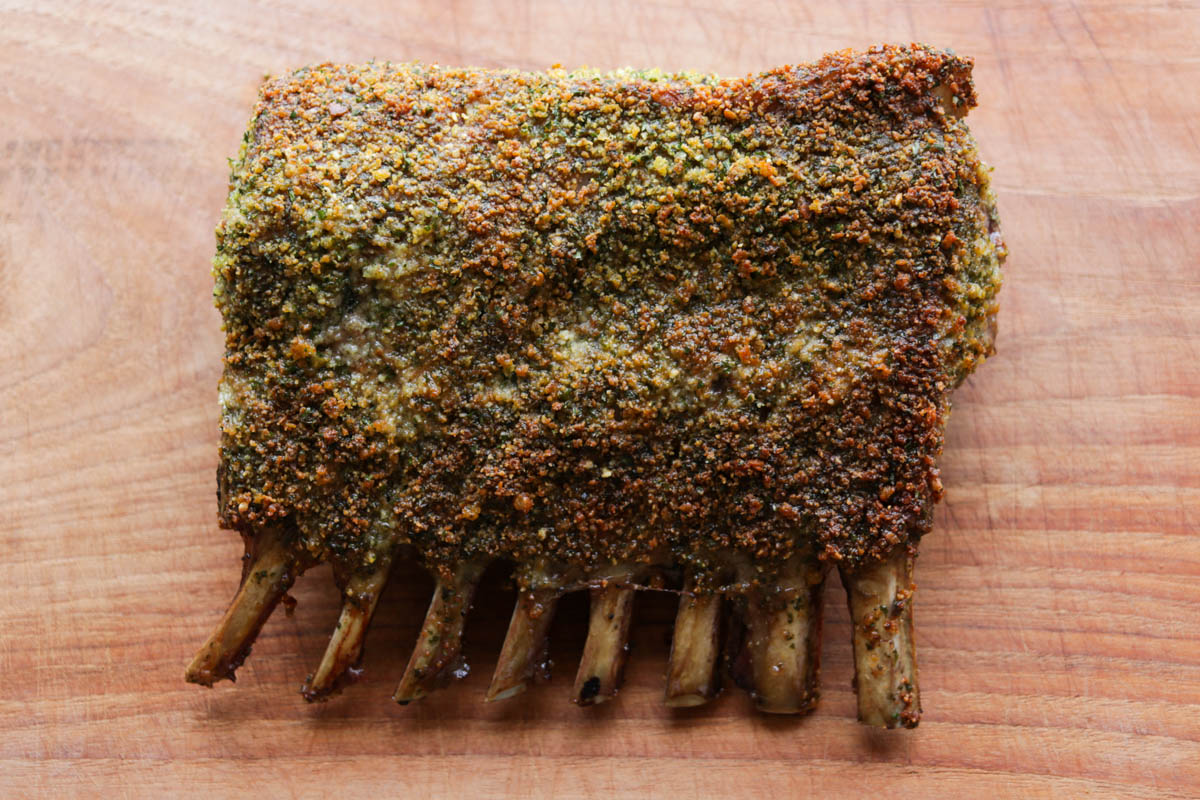 Cooked herb crusted rack of lamb resting on a board