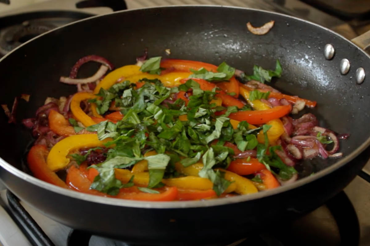 Adding basil to the cooked red onion and peppers 
