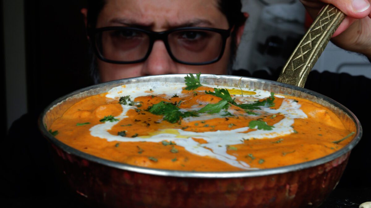 Sahil next to a pan of butter chicken